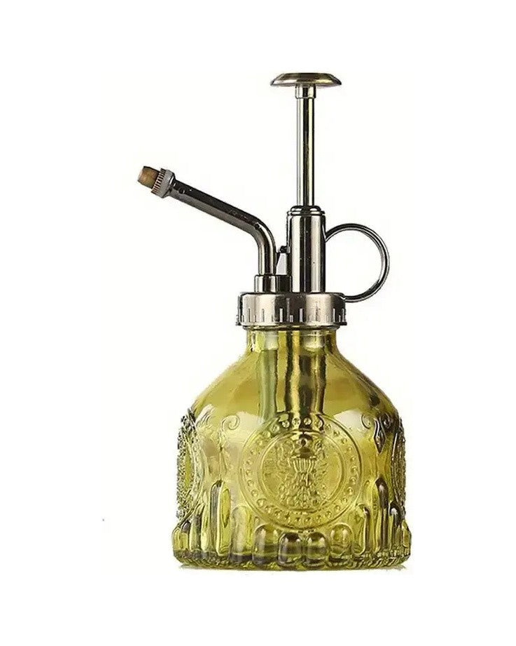 Green pressed glass plant mister with a bronze-tone pump top, on white