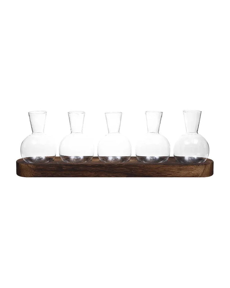 Five round glass bulb vases on a dark wooden tray, on white